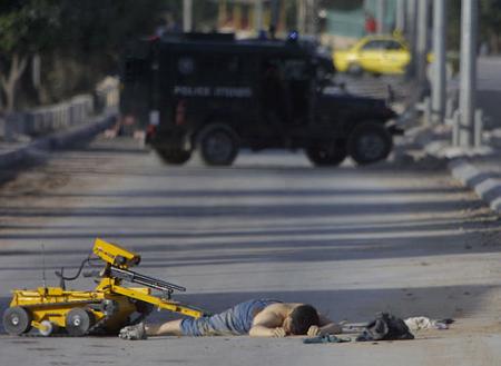 An Israeli bomb squad robot equipped with video camera and a rifle handles the body of a dead Palestinian man, Bethlehem's Jerusalem checkpoint, May 13, 2002.