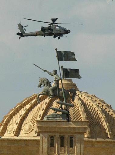 A U.S. Army helicopter gunship patrols by a monument, which Saddam Hussein had built of himself in a heroic pose, entrance to Saddam's palace, Tikrit, Iraq, April 28, 2003.