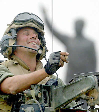 Marines Staff Sgt. Nick Popadich of the 3rd Battalion, 4th Marines Regiment, enjoys a cigar standing on top of his tank, as he arrives at a main crossroad in downtown Baghdad. Saddam's huge statue appears in the background just before destroying it, April 9, 2003.
