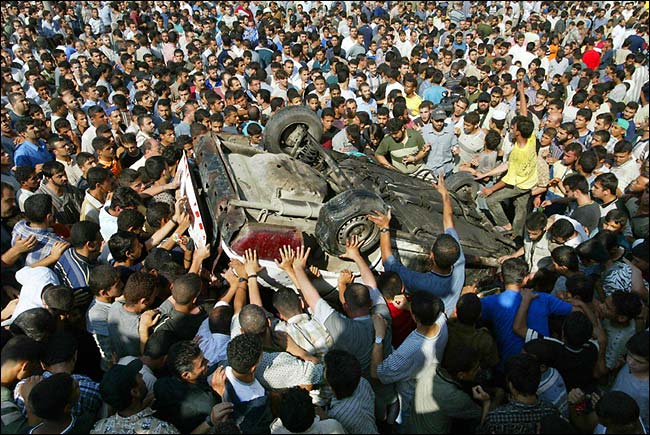 Palestinians protest around a car hit by Israeli missiles, Gaza, June 12, 2003.