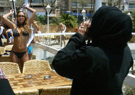 An Arab woman wearing 'niqab' snaps a souvenir photograph of Kristina Nikolayeva, a contestant from Belarus, at the first Lebanon's Miss Bikini contest, Mediterranean coastline, Beirut, July 22, 2003.