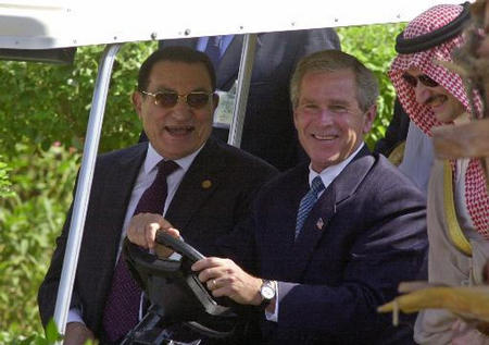 President George W. Bush drives a golf cart taking himself, Egyptian President Hosni Mubarak and other Arab leaders (unseen) to a make a statement while Prince Al-Walid bin Talal appears to the right, Sharm A-Sheik, June 3, 2003.