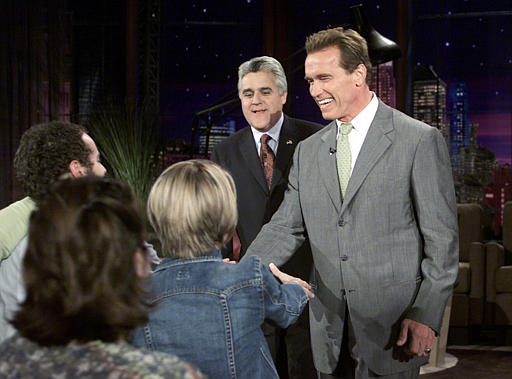 Governor-elect Arnold Schwarzenegger, greets audience members as host Jay Leno looks on after he walked on stage surprising the audience at the end of Leno's monologue during taping of The Tonight Show with Jay Leno, October 8, 2003, Burbank, California.