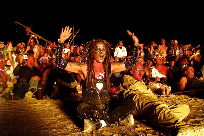 Burners, expressing themselves in wildly free-spirited ways, shout 'Burn the Man!' and the 77-foot-high, skeletal neon-colored Man disappeared beneath a pyre that swirled more than 150 feet into the dusty desert air, Burning Man festival, Black Rock Desert, Nevada, August 31, 2003.