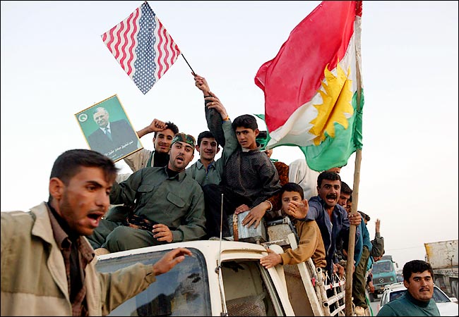 Celebrating the capture of Saddam Hussein, a group of Kurds hold up a Kurdish and an American flags and a picture of Jalal Talabani, the representative of the Patriotic Union of Kurdistan on the Iraqi Governing Council, Tuz Khurmato, Iraq, December 2003.