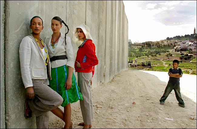 An angry Palestinian boy looks while models from an Israeli fashion house posed along the barrier between East Jerusalem, at right, and the West Bank, Jerusalem, March 3, 2004.