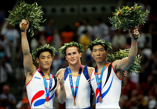 Paul Hamm of the United States, center, after winning the gold medal during the men's gymnastics individual all-around final, and Kim Dae Eun of Korea the silver medalist on the left, and Yang Tae Young of Korea the bronze medalistat, the 2004 Summer Olympic Games, Athens, August 18, 2004.