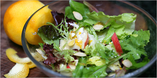 A salad made with sliced apples, cranberries and goat cheese is salted with toasted pumpkin seeds.