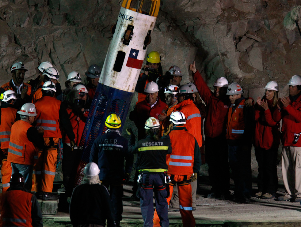 Chile's President Sebastián Piñera, in red jacket next to the capsule, and other officials and rescue workers talk as rescue worker Manuel Gonzalez Paves is lowered in the capsule into the mine where miners are trapped to begin the rescue at the San Jose Mine near Copiapo, Chile, October 12, 2010.