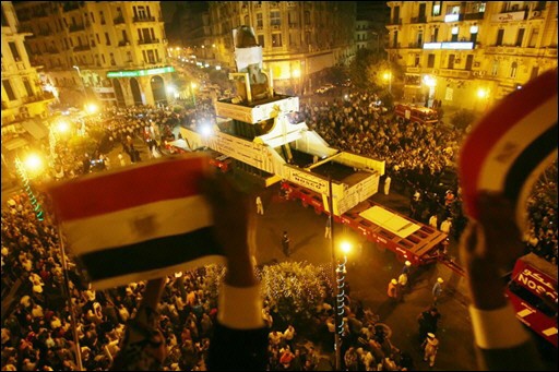 Egyptians wave their national flag from a balcony at Talat Harb Square in the heart of Cairo, as they bid farewell to the 3,200-year-old statue of Pharaoh Ramesses II from a congested square in downtown Cairo to its new home at the under-construction Grand Museum near Giza Pyramids, early August 25, 2006.