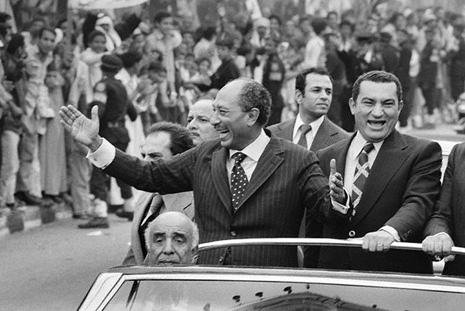 Egyptian President Anwar A-Sadat (L) waving to a crowd as Vice-President Hosni Mubarak laughs beside him in a convertible vehicle, c. 1975. 